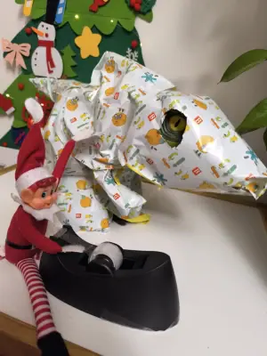 Elf wraps up a dinosaur in festive paper for Christmas surprise